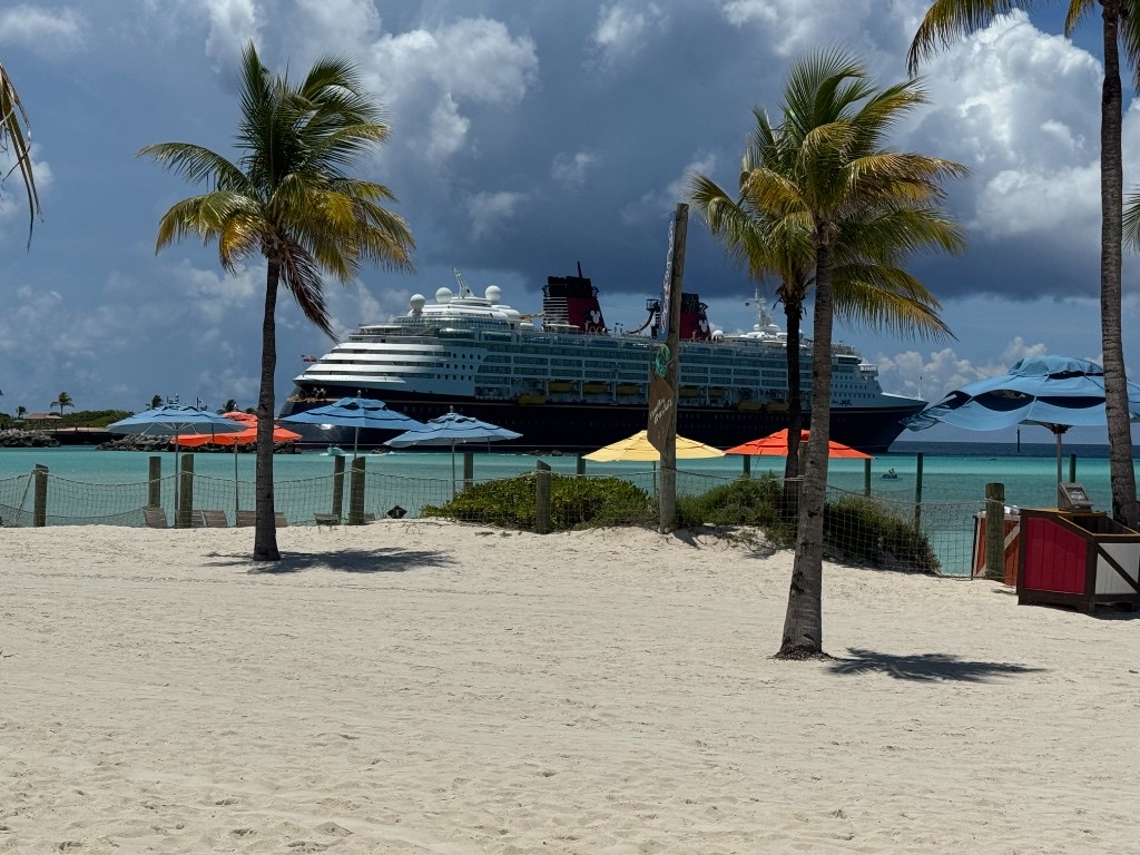 Dream-class Disney ship seen from Castaway Cay beach with palm trees and umbrellas